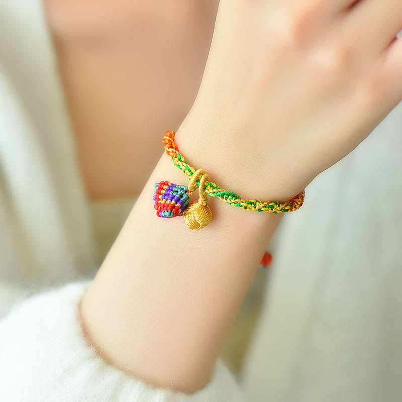 Colorful braided bracelet with a heart charm on a wrist against a neutral background