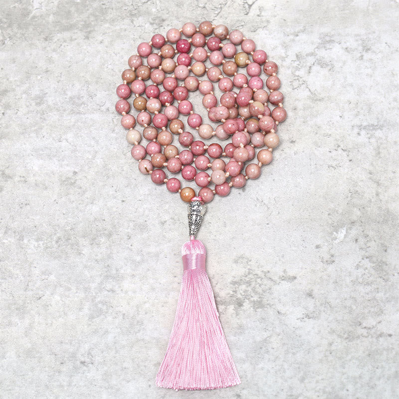 Mala necklace with pink beads and tassel on a textured gray surface