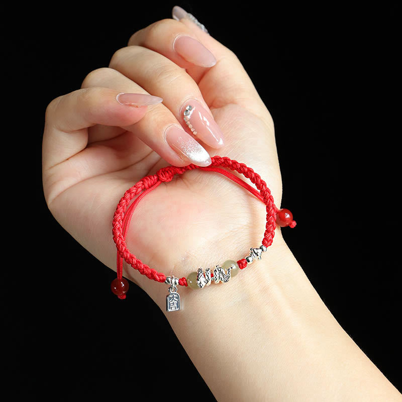 Hand wearing a red string bracelet with silver charms on a black background