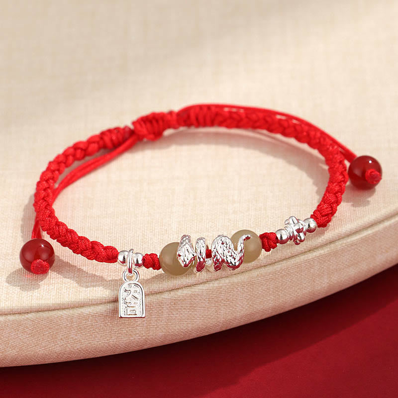 Red string bracelet with silver charms on a beige surface