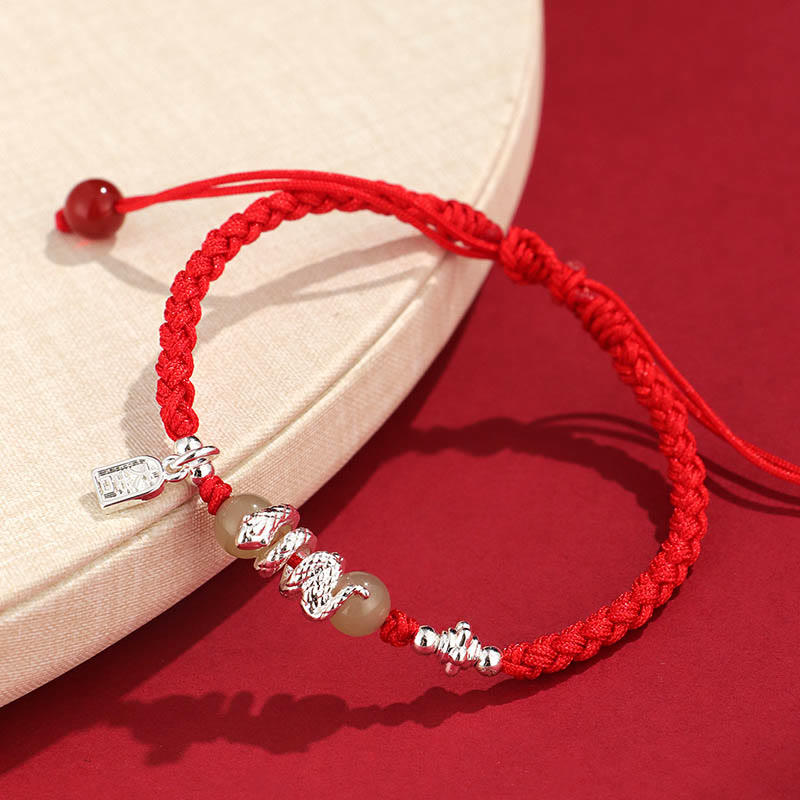 Red braided bracelet with silver charms on a red background