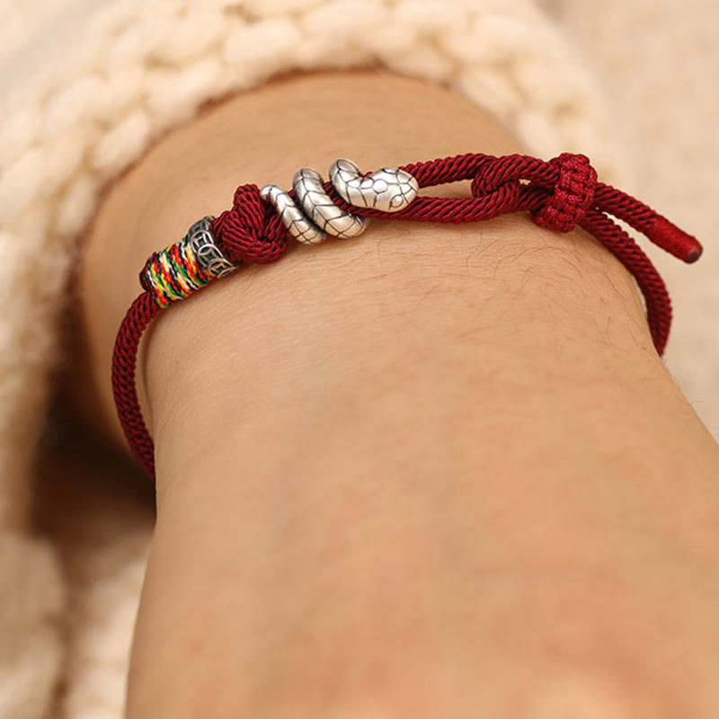 Red bracelet with silver and colorful beads on a wrist against a neutral background