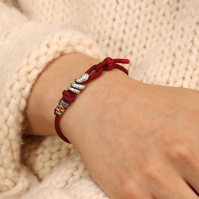 Red bracelet with silver beads on a wrist against a beige textured background