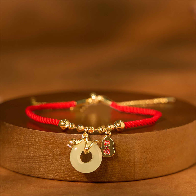 Bracelet with red string and gold charms on a wooden surface