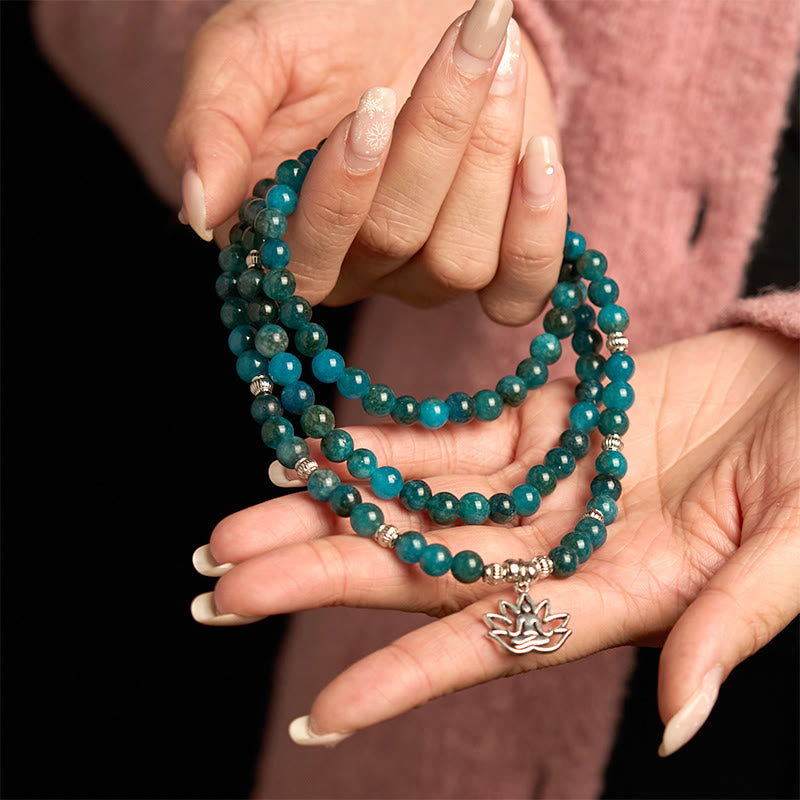 Teal beaded bracelets with a silver charm held in hands against a dark background