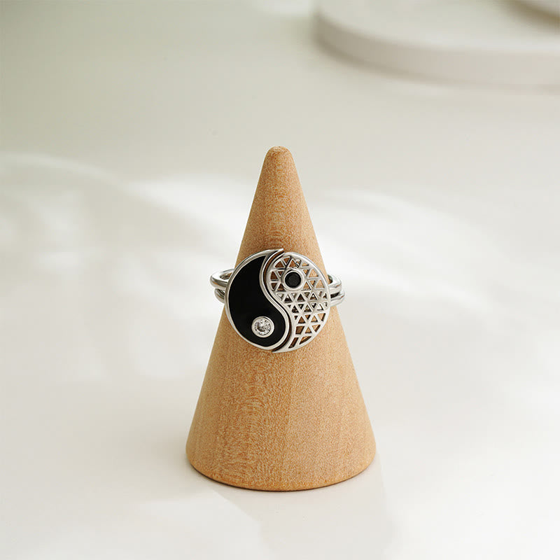 Silver ring with a black yin yang symbol on a beige cone-shaped stand against a white background