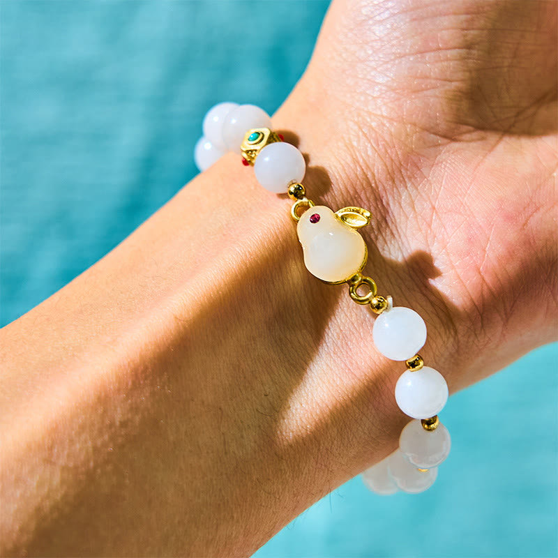 Close-up of a wrist wearing a bracelet with white beads and gold accents against a blue water background