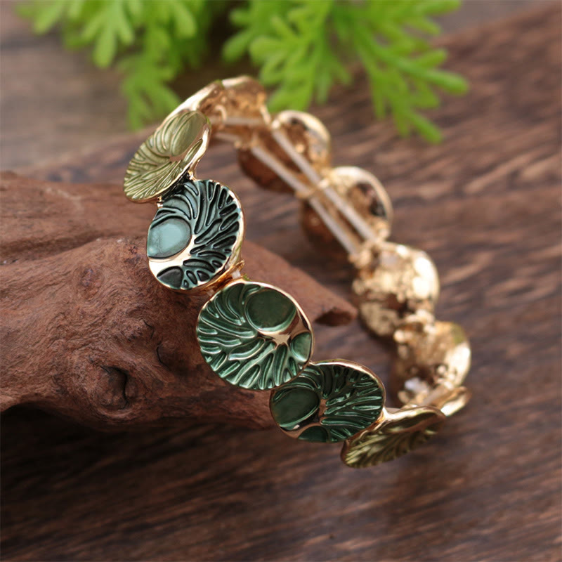 Gold and green bracelet on a wooden surface with green leaves in the background