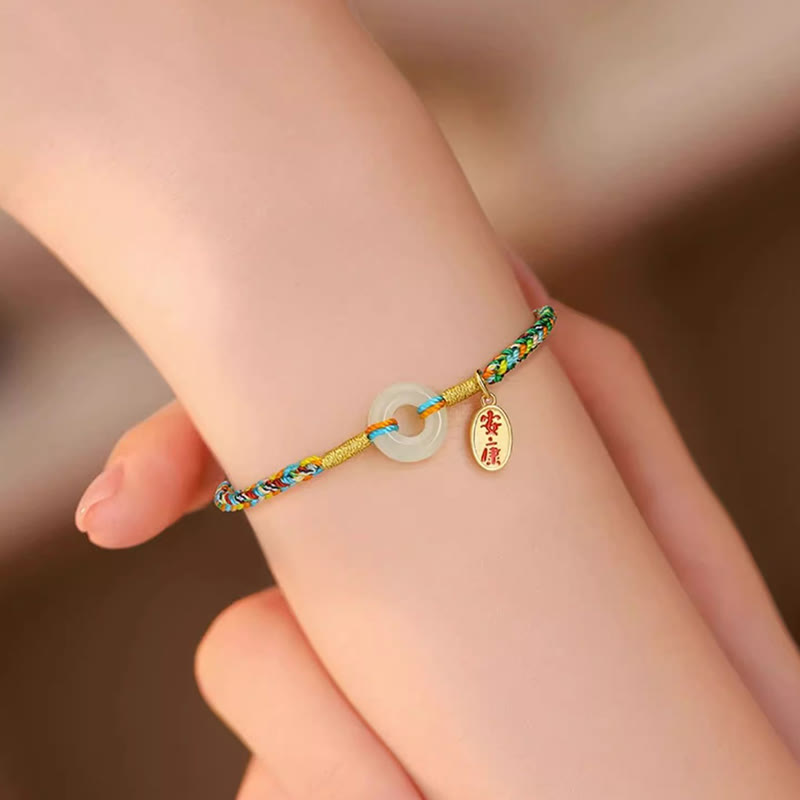 Colorful braided bracelet with a round charm on a wrist against a blurred background