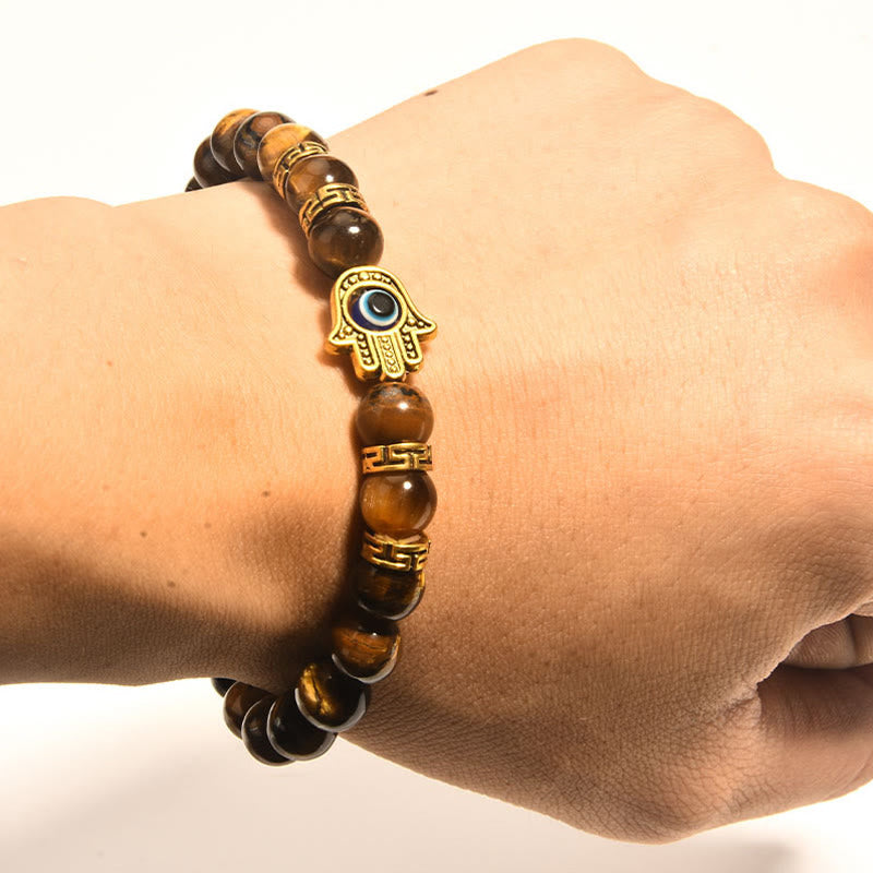 Hand wearing a tiger eye bracelet with a gold Hamsa hand charm on a white background