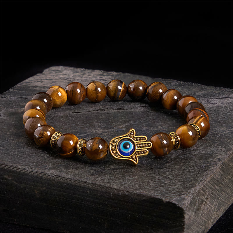Brown beaded bracelet with a gold Hamsa hand charm on a dark stone surface