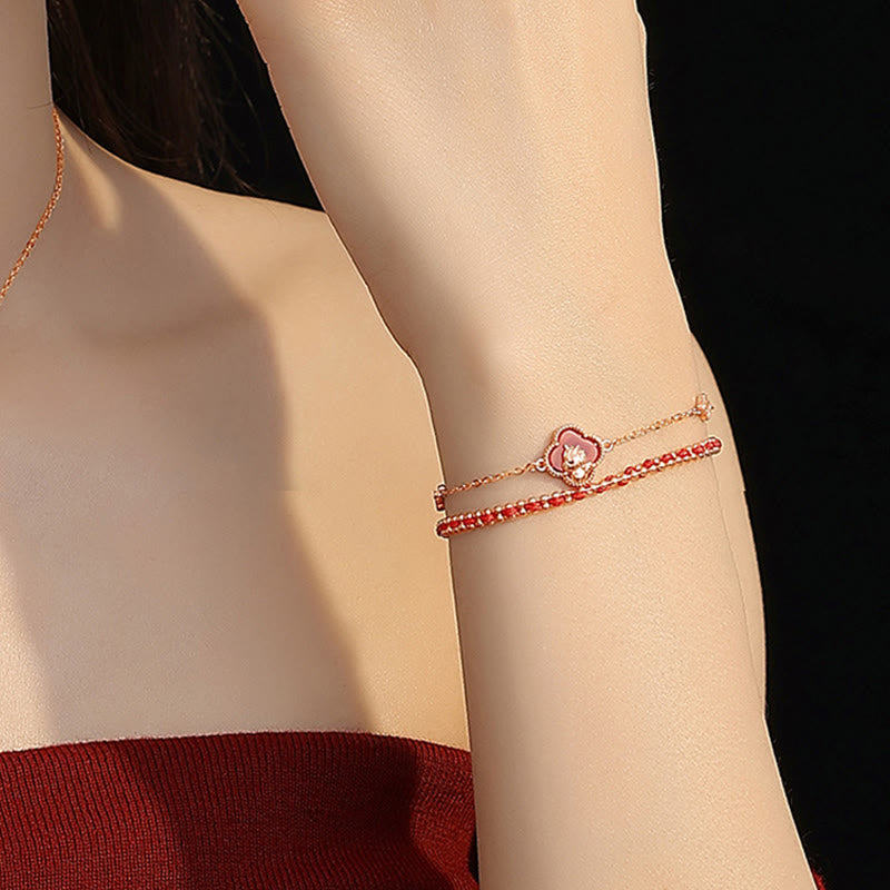 Close-up of a person's arm wearing a delicate bracelet with a floral charm on a dark background