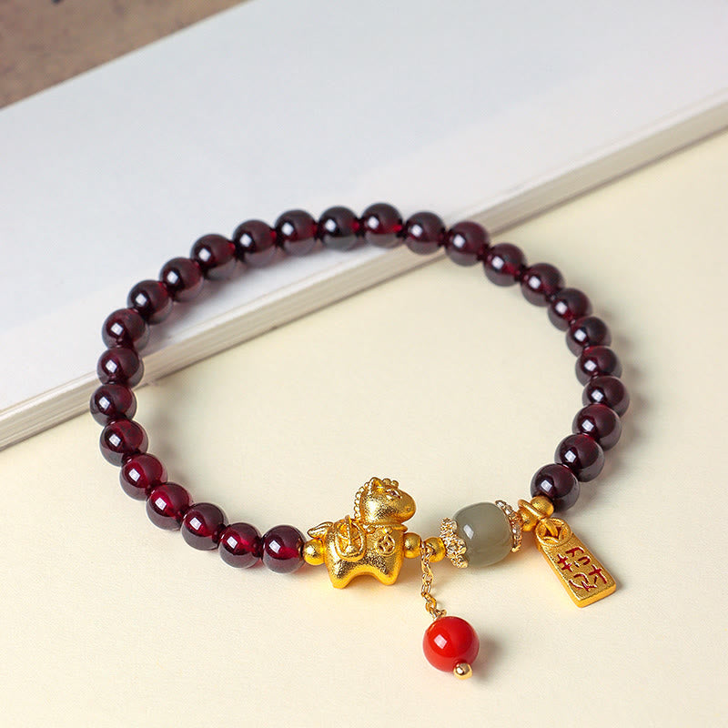 Garnet beaded bracelet with gold and red charms on a white surface