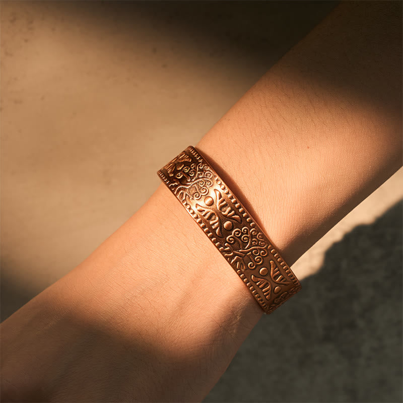 Bronze bracelet with intricate patterns on a wrist against a neutral background