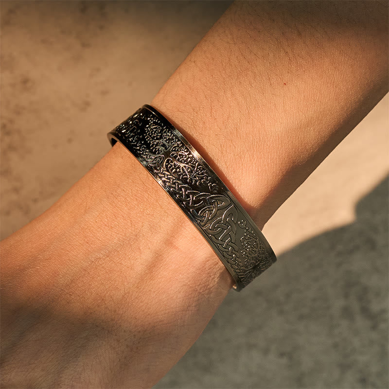 Close-up of a person's wrist wearing an ornate black bracelet against a neutral background