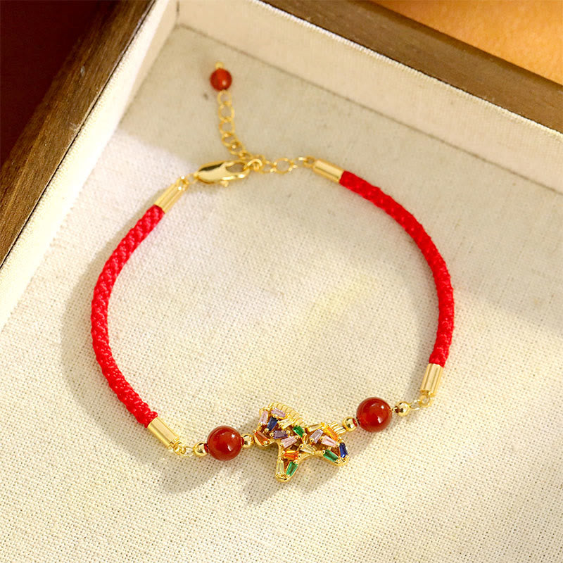 Red bracelet with gold accents and a decorative charm on a light fabric surface.