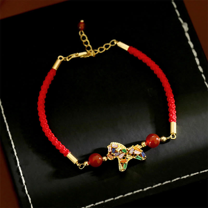 Red string bracelet with gold accents and a colorful charm on a black background