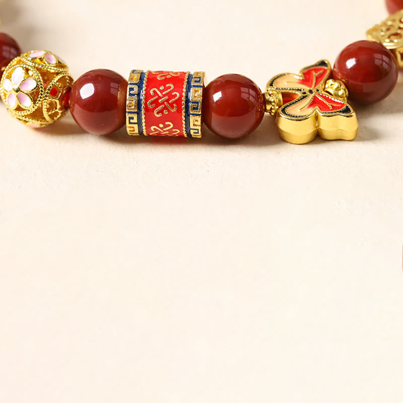 Decorative bracelet with red beads and gold accents on a beige background