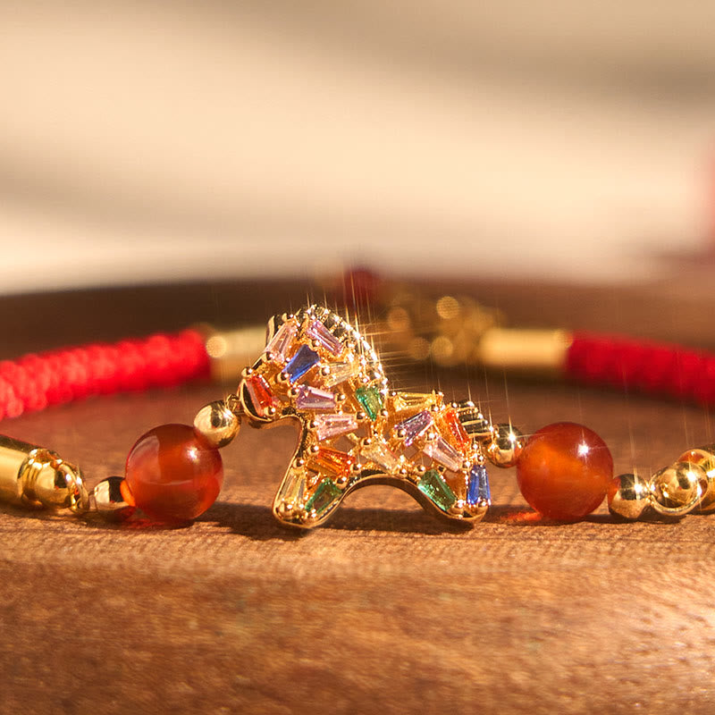 Colorful horse-shaped brooch on a red and gold necklace with a blurred background