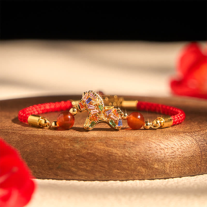 Bracelet with a gold horse charm on a wooden surface with red flowers.