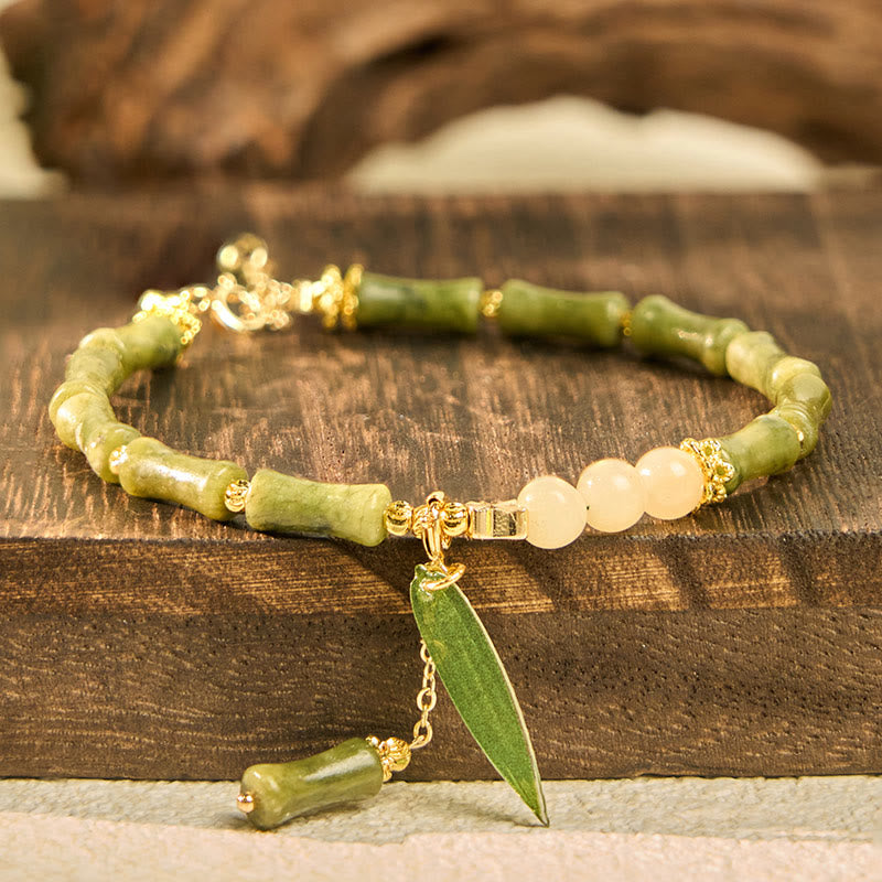 Green beaded bracelet with gold accents and a leaf charm on a wooden surface