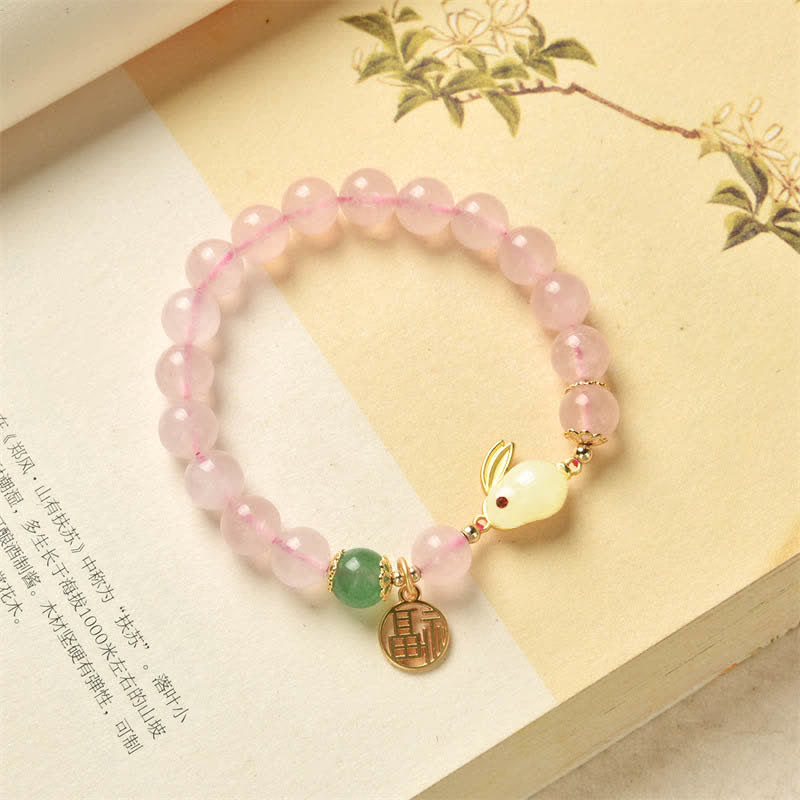 Pink beaded bracelet with gold charm and green gemstone on a decorative background