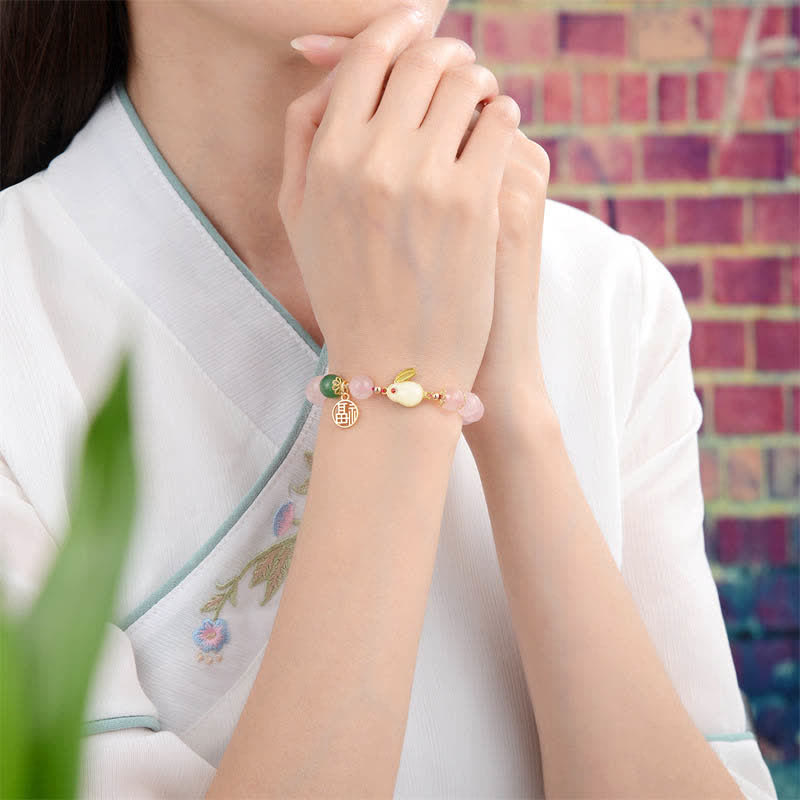Person wearing a bracelet with colorful beads and gold accents, sitting against a blurred background.