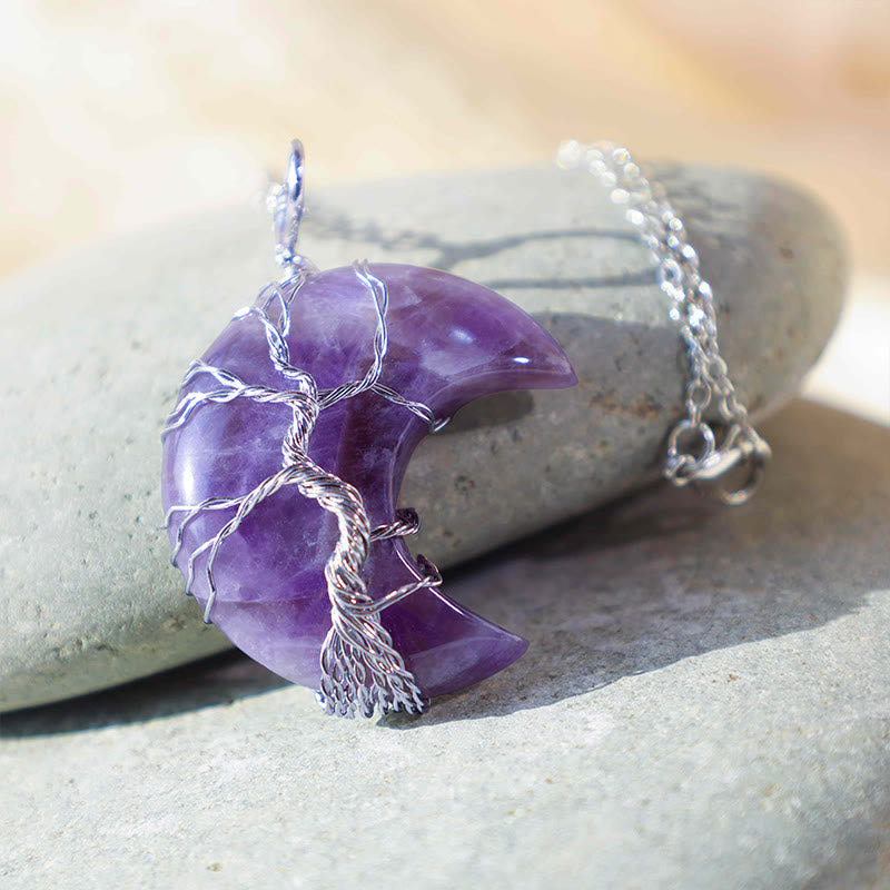 Purple amethyst necklace with silver tree design on a stone surface