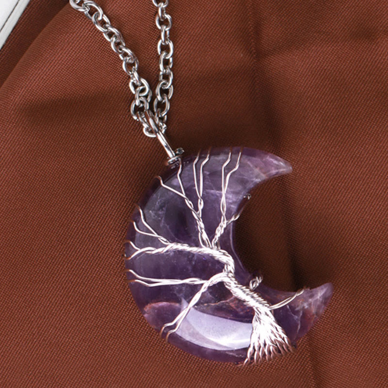 Amethyst moon-shaped pendant with silver tree design on a brown fabric background