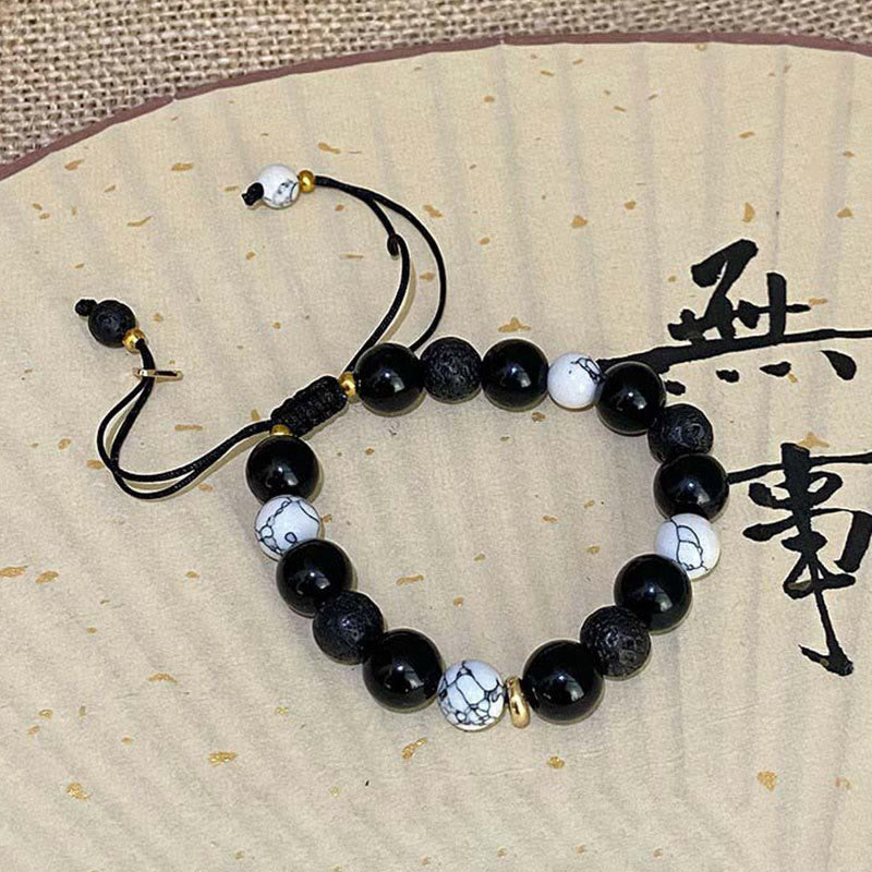 Black beaded bracelet with white accents on a textured beige background