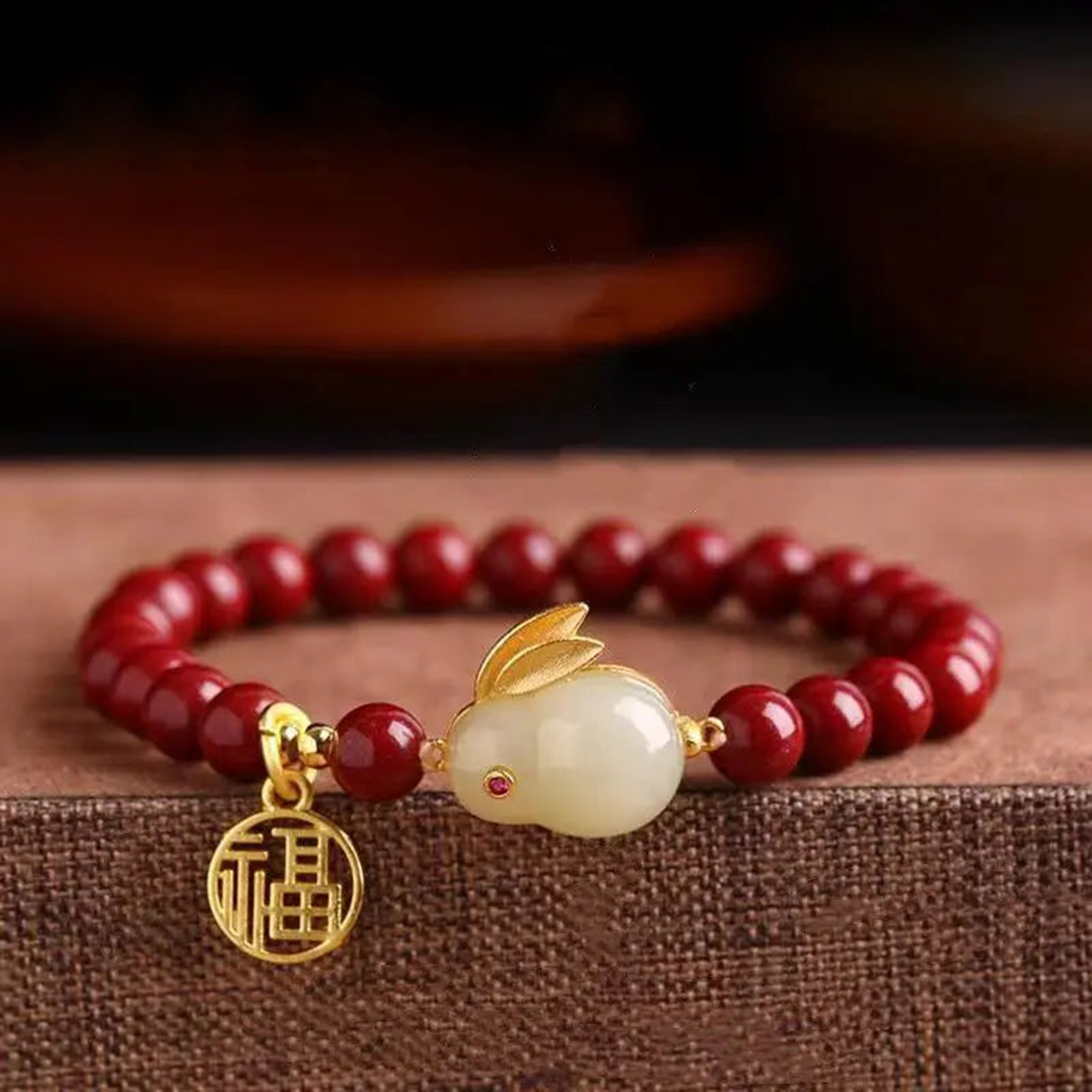 Red beaded bracelet with a gold charm and rabbit figure on a brown surface