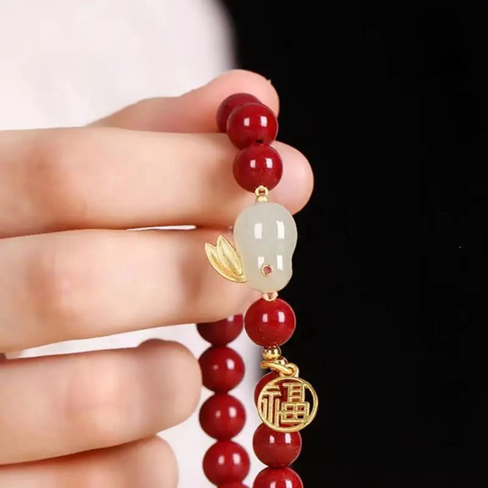 Red beaded bracelet with gold and white charms held by a hand against a black background