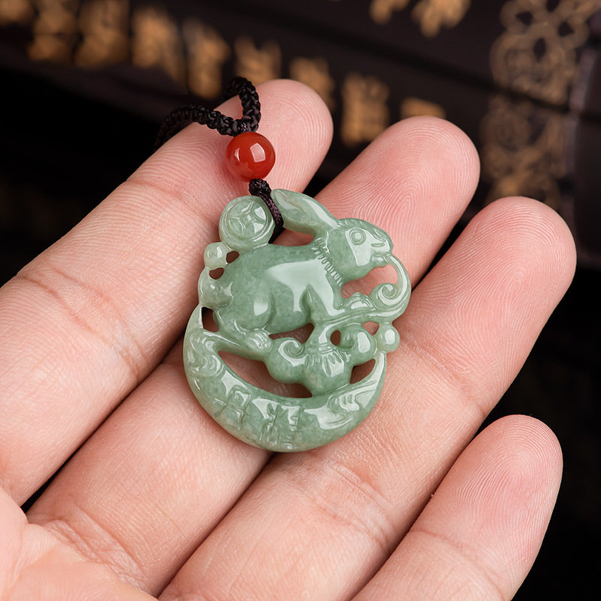 Green jade pendant with rabbit design held in a hand against a dark background