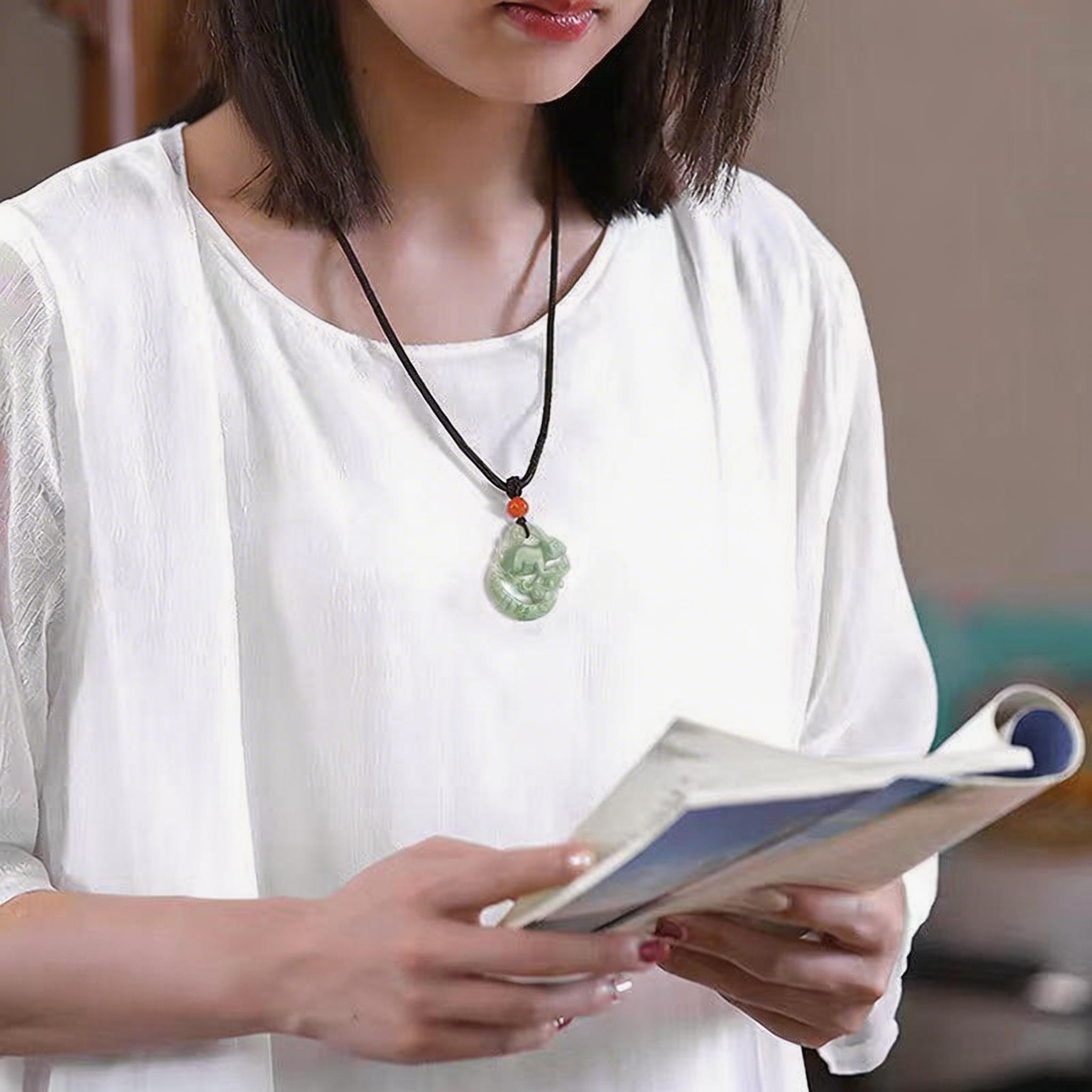 Woman wearing a white shirt and a necklace with a green pendant, holding a book.