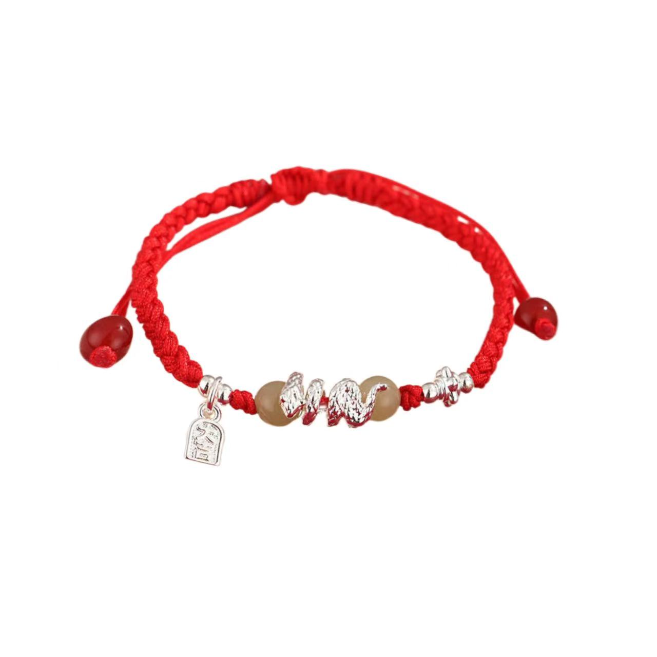 Red bracelet with silver and gold charms on a white background