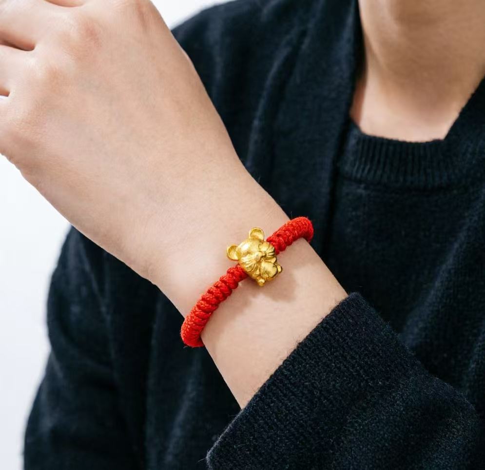 Red string bracelet with a gold charm on a person's wrist against a black sweater background