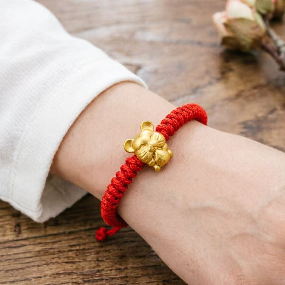Red string bracelet with a gold charm on a wrist against a wooden background