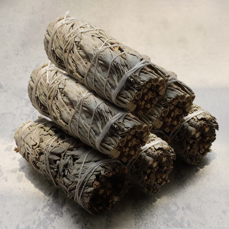 Stack of tied sage smudge sticks on a light gray surface
