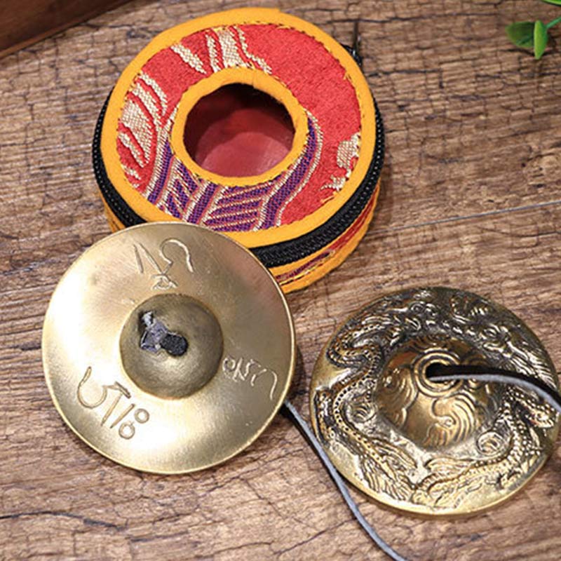 Two brass cymbals on a wooden surface with a decorative container.
