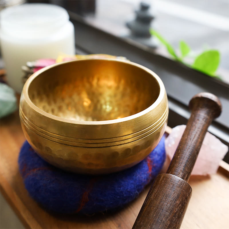 Gold singing bowl with wooden striker on a blue cushion