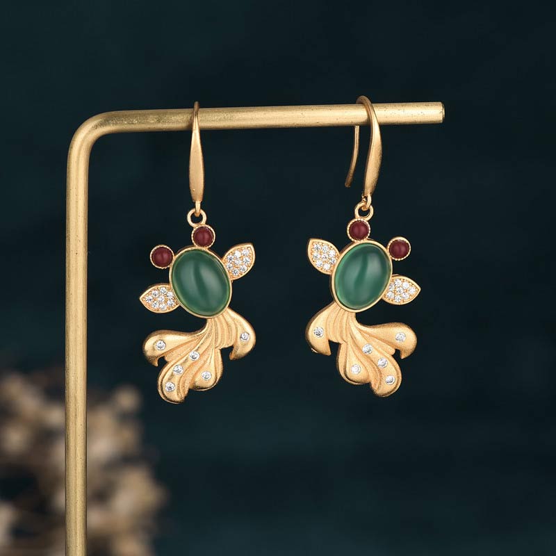 Gold earrings with green gemstones and red accents on a dark background