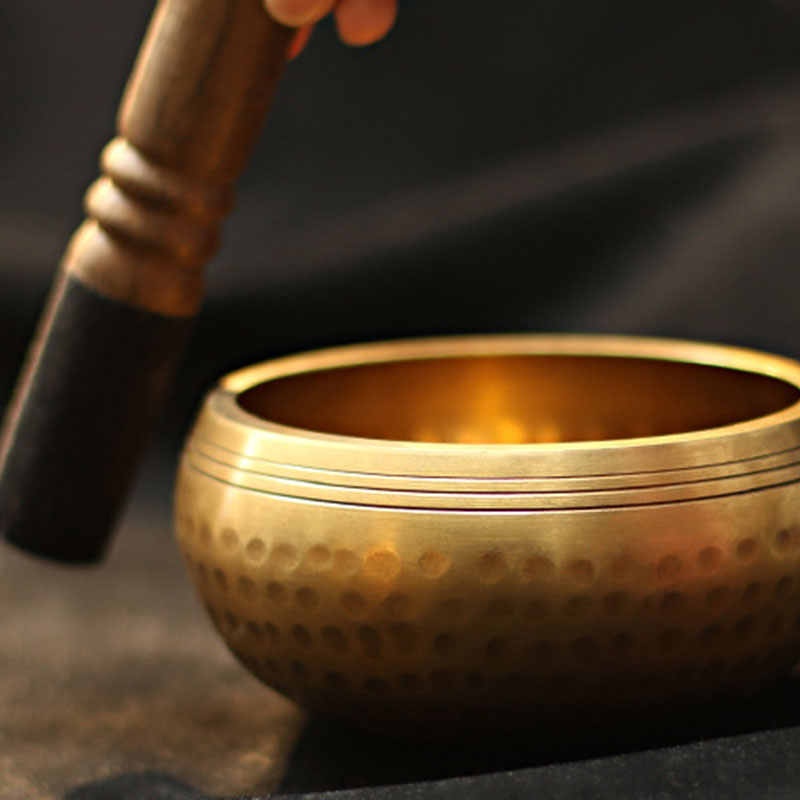 Gold singing bowl with a wooden mallet on a dark background