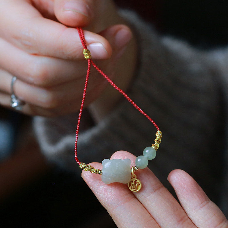 Hand holding a red string bracelet with a jade bear charm and gold accents.