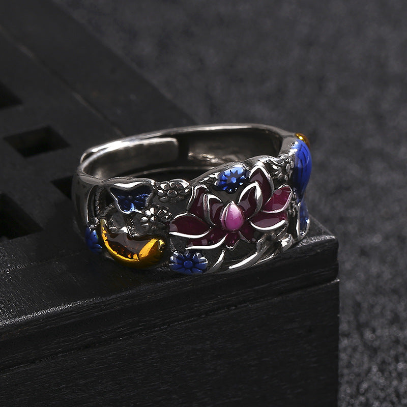 Silver ring with floral design and colored stones on a black surface