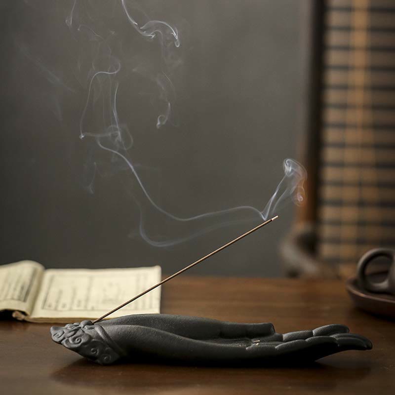 Incense stick with smoke rising from a hand-shaped incense holder on a wooden surface.