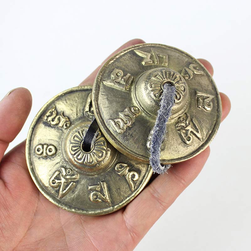 Two brass meditation chimes held in a hand against a white background