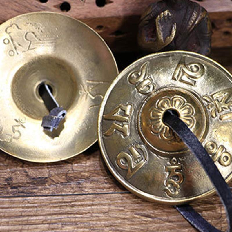 Two brass cymbals with engraved designs on a wooden surface