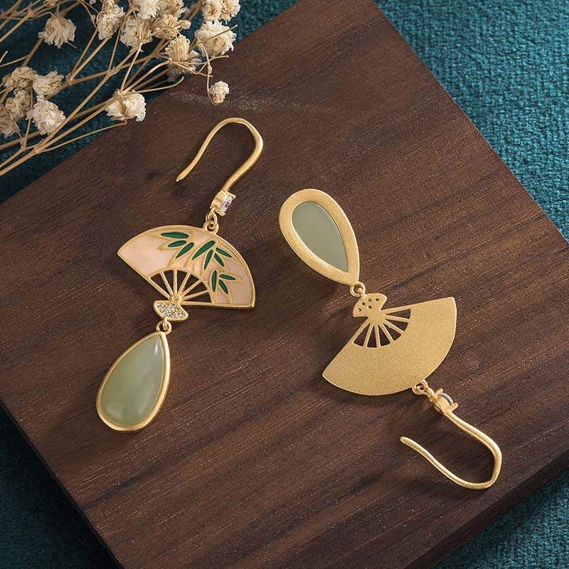 Gold earrings with green teardrop stones on a wooden surface