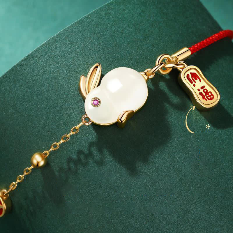 Gold bracelet with rabbit charm and red string on a green background