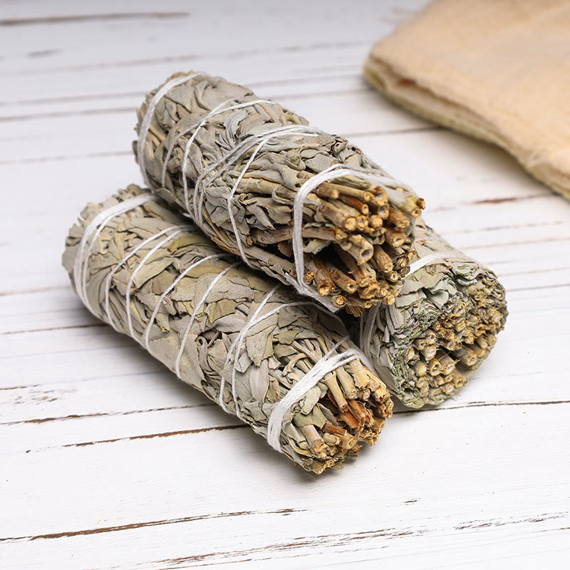 Two bundles of sage tied with white twine on a wooden surface